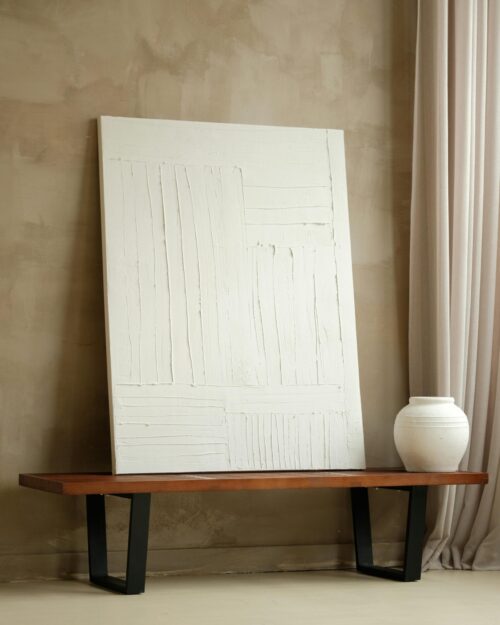 Elegant minimalist interior featuring a textured white canvas and ceramic vase on a wooden bench.